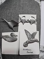 Four pewter brooches displayed together showing bird and fish designs.