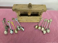 Photo showing wooden butter press and assortment of souvenir spoons laid out on pink fabric