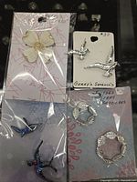 Four antique brooches displayed in package with paper backing: single white magnolia flower, two silver-tone seagulls, and two silver-tone leaf wreath brooches.