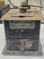 Front and top view of the Antique Universal Coffee Mill showing the brand label, patent date, and overall condition with rust and wear.