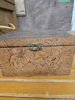 Front view of antique wooden box showing metal latch and vine leaf pyrography design