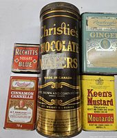 Five vintage tins arranged close together on a white surface: Christie’s Chocolate Wafers cylindrical tin, Rawleigh’s Ginger and Cinnamon tins, Keen’s Mustard tin, and Reckitt’s Square Blue tin in package.