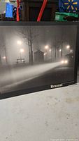 Full view of the Brassai lighted printed wall art showing the urban foggy street scene with illuminated lamps and trees in black and white.