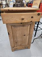 Front view of wooden cupboard with drawer partially open showing natural wood and a knob.