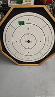 Octagonal crokinole game board with concentric scoring rings and center hole. Light wood frame. White background with black markings.