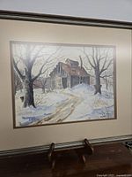 Framed watercolor artwork showing a rustic sugar shanty in winter scenery with snow and trees.