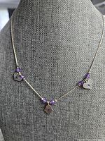 Full view of the silver necklace displayed on a grey necklace stand showing the Hamsa hand pendant, heart charms and amethyst beads on a fine silver chain.