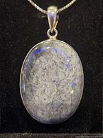 Front close-up of oval dendritic opal pendant in sterling silver setting on chain.