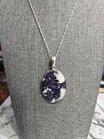Front view of oval Lepidolite pendant on display stand showing purple and white pattern.