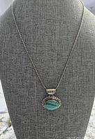 Front view of the necklace on a grey fabric display bust showing the chain and oval malachite pendant.