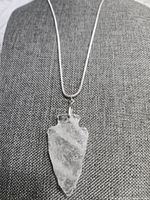 Front view of the quartz arrowhead pendant on the silver chain displayed against a grey fabric background.