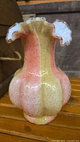 Front view of a bulbous spangle glass vase with pink and yellow stripes, scalloped ruffled rim with missing piece.