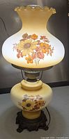 Full view of the vintage hurricane table lamp showing ruffled top glass shade with floral design and yellow glass base on ornate metal stand