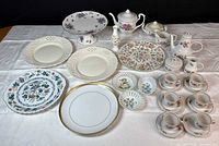 Wide shot showing whole assorted china lot including Hammersley cake plate on pedestal, Minton bud vase and matching plate, various plates, floral teapot, sugar bowl, creamer, and teacups with saucers.