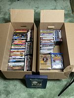 Photo of two large cardboard boxes filled with assorted DVDs showing variety of movie titles and series.