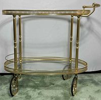 Full front view of brass bar cart showing both oval glass shelves, frame and wheels