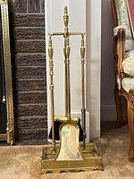 Full view of the fireplace tool set against wall and carpet, showing tools hanging on stand with detailed finial handle design and openwork base.