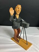 Front-side view of the hand-carved wooden photographer figure with camera setup, showing raised hand and detailed clothing.