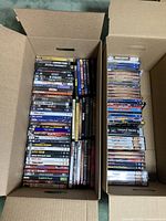 Two open cardboard boxes filled with stacked DVD cases by title spines