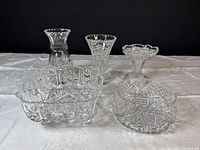 Three crystal vases and two crystal bowls displayed together on white cloth with black background.