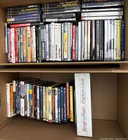 Box with a large collection of DVD musical titles stacked with varied colors and visible titles.