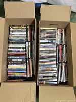 Two open boxes filled with a variety of DVD movies laid upright to show spines. Shows overall quantity and selection of titles.