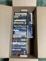 Cardboard box filled with stacked DVDs showing spines from top view