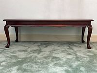 Full front view of the rectangular coffee table showing the dark mahogany finish, slightly curved cabriole legs, and decorative apron beneath the tabletop.