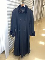 Full length photo of the black double breasted winter coat with fur collar and cuffs on a hanger.