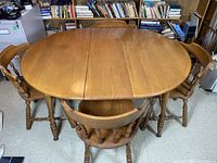 Maple oval dining table with 4 matching spindle-back chairs, shown assembled with leaf inserted.