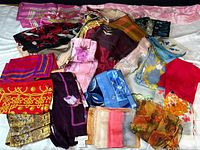 Wide shot of the assortment of 19 scarves spread out showing colors and variety of fabrics and patterns.