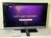 Sony Bravia LCD TV powered on showing language selection screen. Includes remote and manuals.