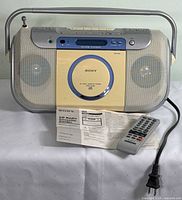Front view of Sony CFD-E100 CD Radio Cassette-Corder with remote control and instruction manual in front, power cord visible.