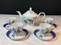 Top view showing the full set of one tea pot, four cups, and four saucers on white surface with black background