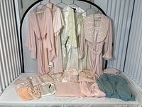 Overview of five pastel robes hanging on rack and multiple folded loungewear items and slippers on table