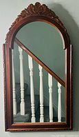 Front view of vintage mirror hung against wall showing detailed hand-carved floral motif on arched top wooden frame and clear reflective glass.