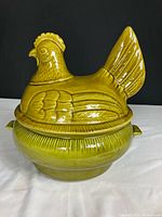 Front view of vintage green nesting hen soup tureen with detailed feathers and comb, placed on white surface