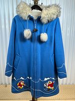Full front view of light blue parka on hanger showing hood, fur trim, front zipper and pom-poms