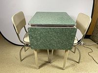 Front view of green laminate drop leaf table with both chairs