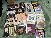 Overview of approximately 30 vinyl LPs arranged on green carpet showing titles and general condition
