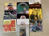 Photo showing 15 vinyl records from Rod Stewart, Queen, and The Mamas & Papas arranged in rows on carpet floor showcasing cover artwork.