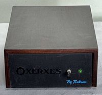 Front view of power supply showing black front panel with ‘Xerxes’ cutout logo, toggle switch, green LED and ‘By Roksan’ script.