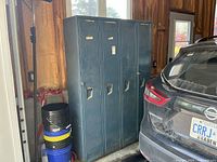 Four tall, blue metal lockers standing side by side indoors next to a vehicle for size reference.