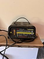 Black Schumacher SF-82-6 manual battery charger with a handle, placed on a wooden surface.