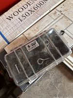 Clear hard plastic box closed, showing screws and hooks inside through the transparent lid