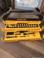 Yellow and black Stanley tool kit with two fold-out trays showing various socket sizes and screwdriver bits, plastic handle for carrying.