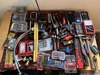 Overview of assorted hand tools including saw blades, drill bit sets, measuring tape, and various screwdrivers and pliers organized on a surface