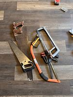 Photo showing two traditional hand saws and one hacksaw on wood floor