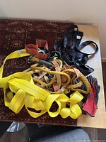 Yellow lifting strap, black safety harness straps, orange slings, rope, and work gloves on a wooden table