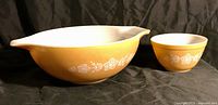 Large yellow Cinderella Pyrex bowl with white floral Butterfly Gold pattern next to smaller matching bowl on a dark background